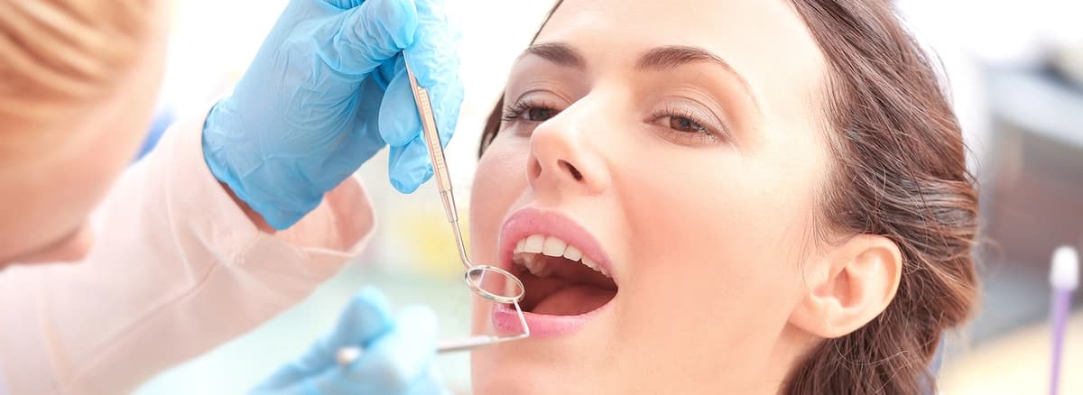 Patient receiving dental exam as emergency dentist Astoria team member in gloves uses dental mirror and scaler.