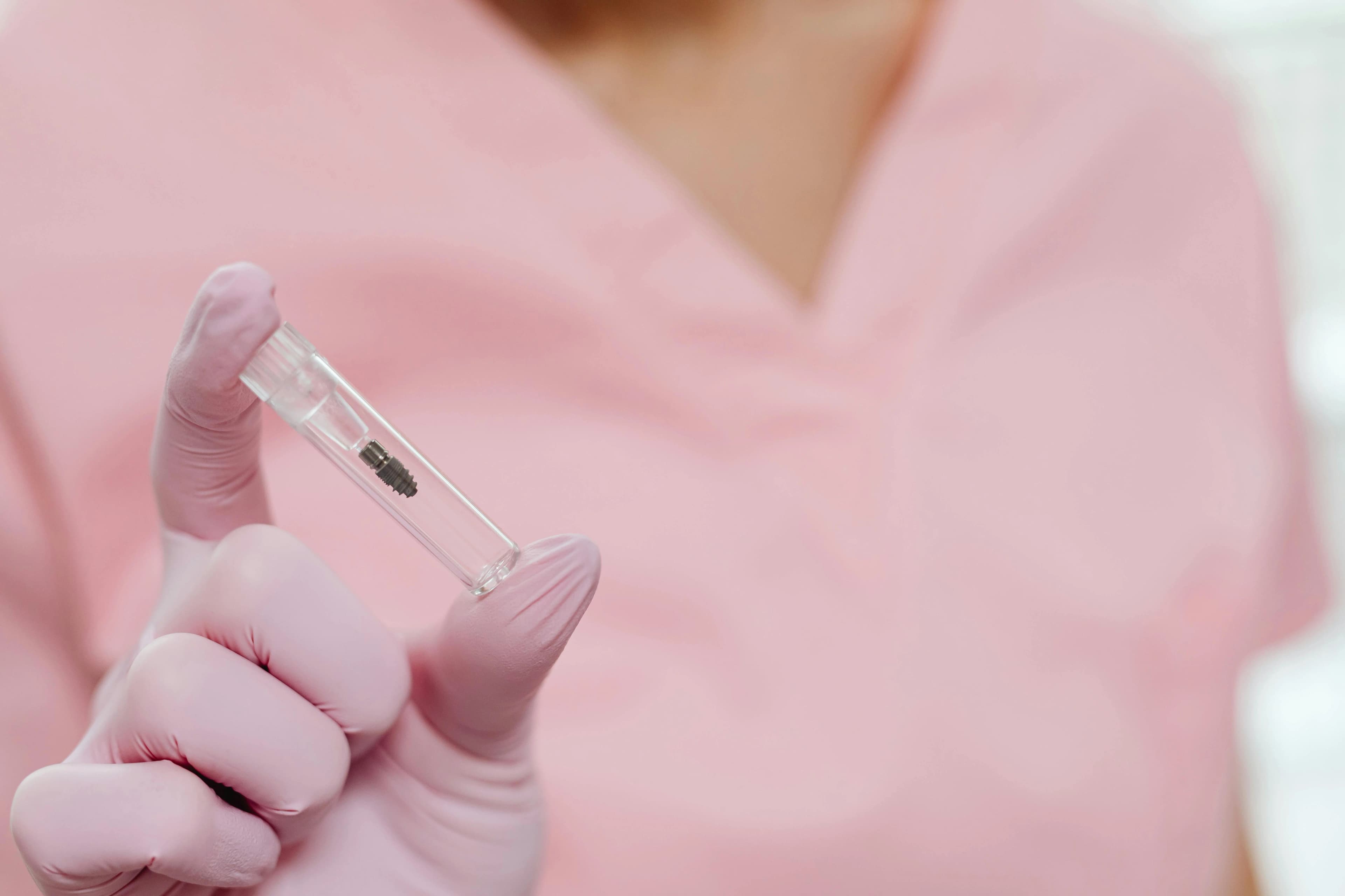 Person wearing pink gloves and scrubs holding a small dental implant inside a clear glass tube