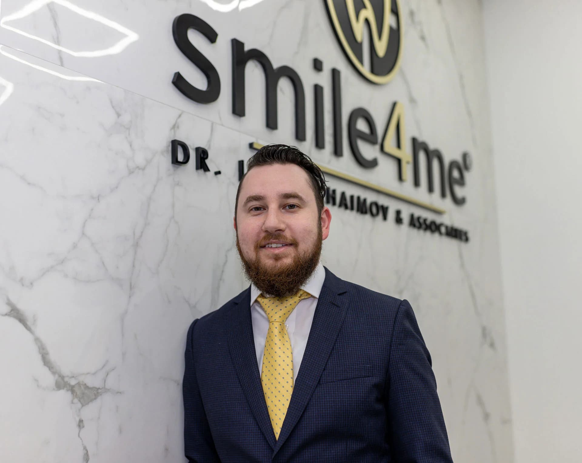Dr. Iosif Khaimov standing beneath the Smile4Me Dental Care office logo