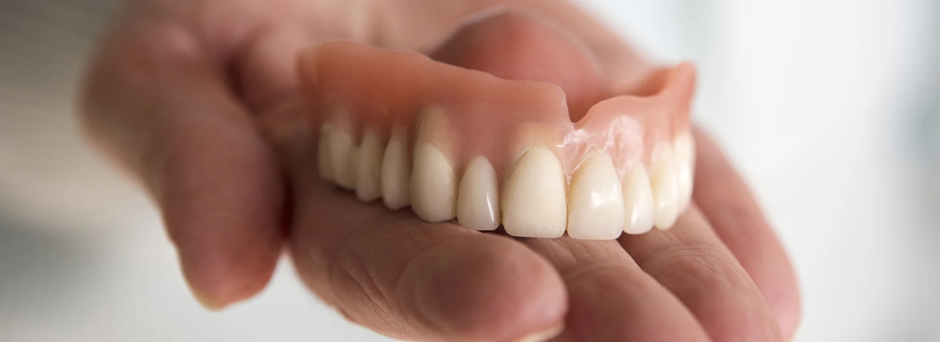 A full denture held in a hand at Smile4Me Dental Care in Astoria