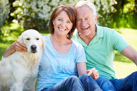 photo-smiling-couple-with-dog-outdoors-discussing-full-mouth-dental-implants-astoria-in-sunny-park-setting