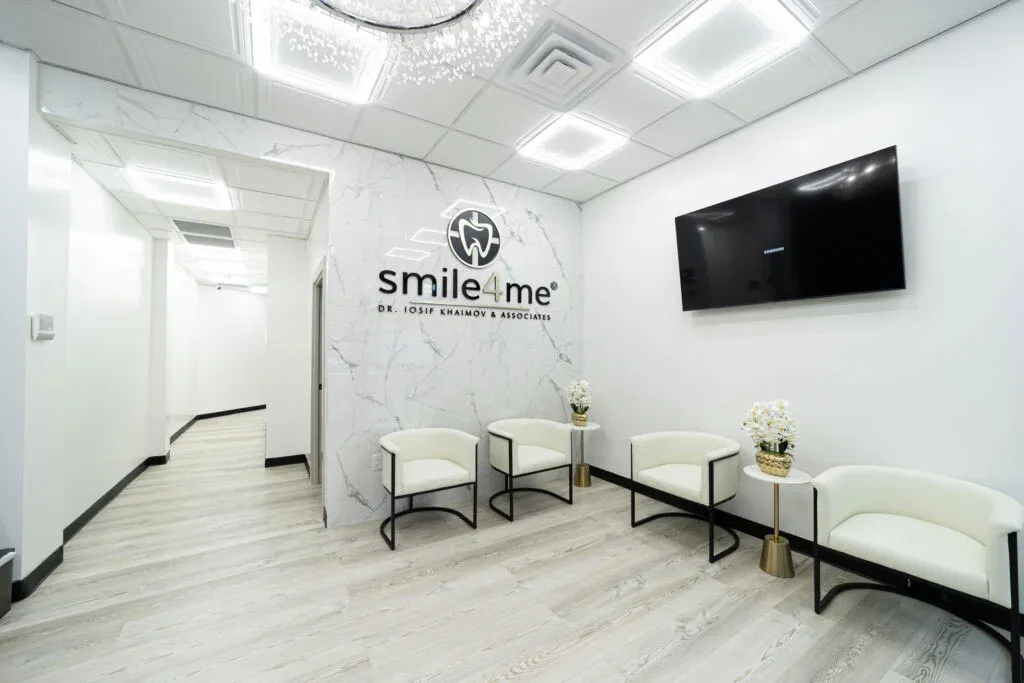 Modern Dental Office Waiting Room With White Chairs Flat Screen Tv Marble Wall And Smile4me Logo Displayed Behind Reception Area